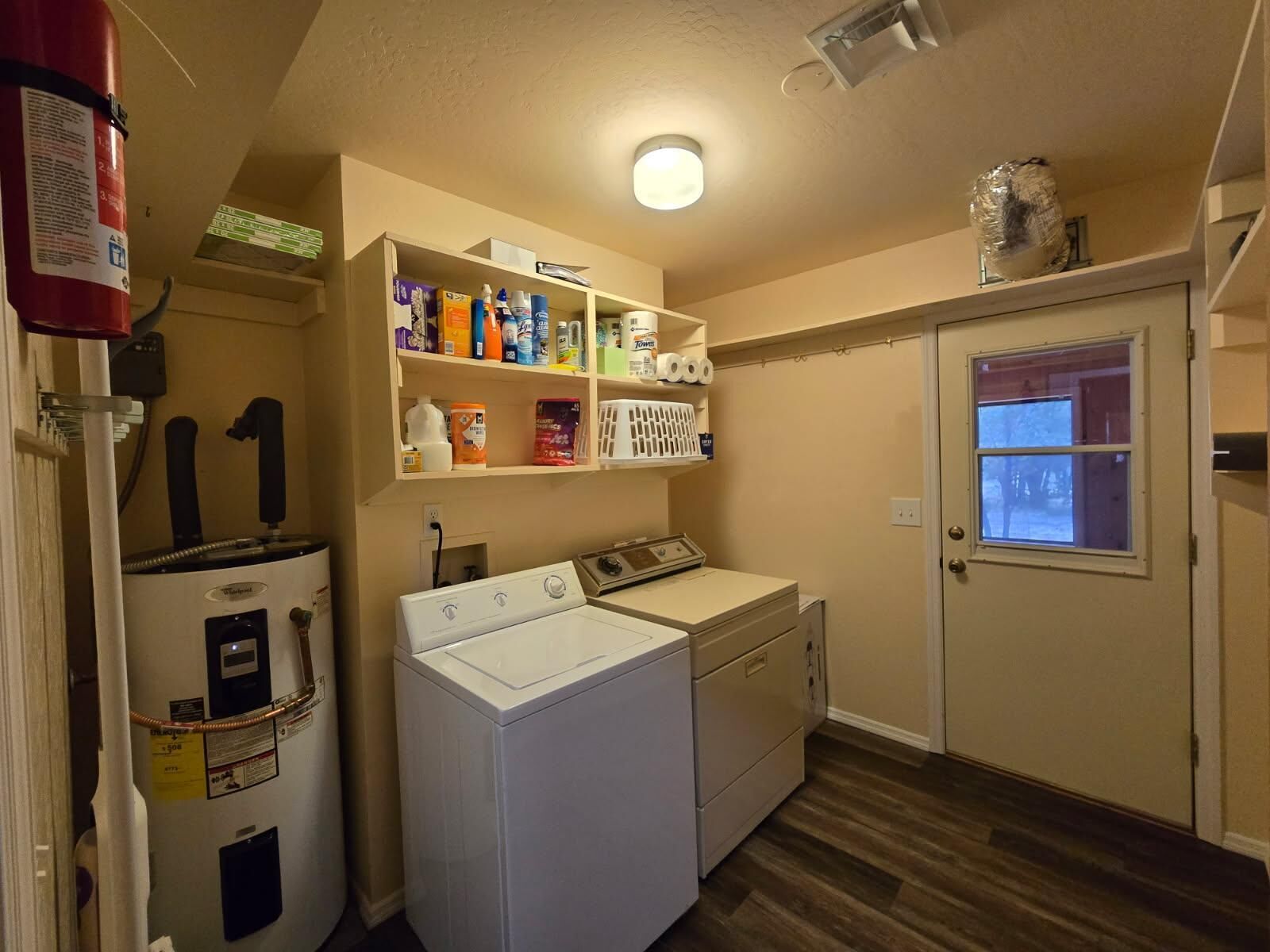 A laundry room with a washer and dryer, shelves with cleaning supplies, and a fire extinguisher.