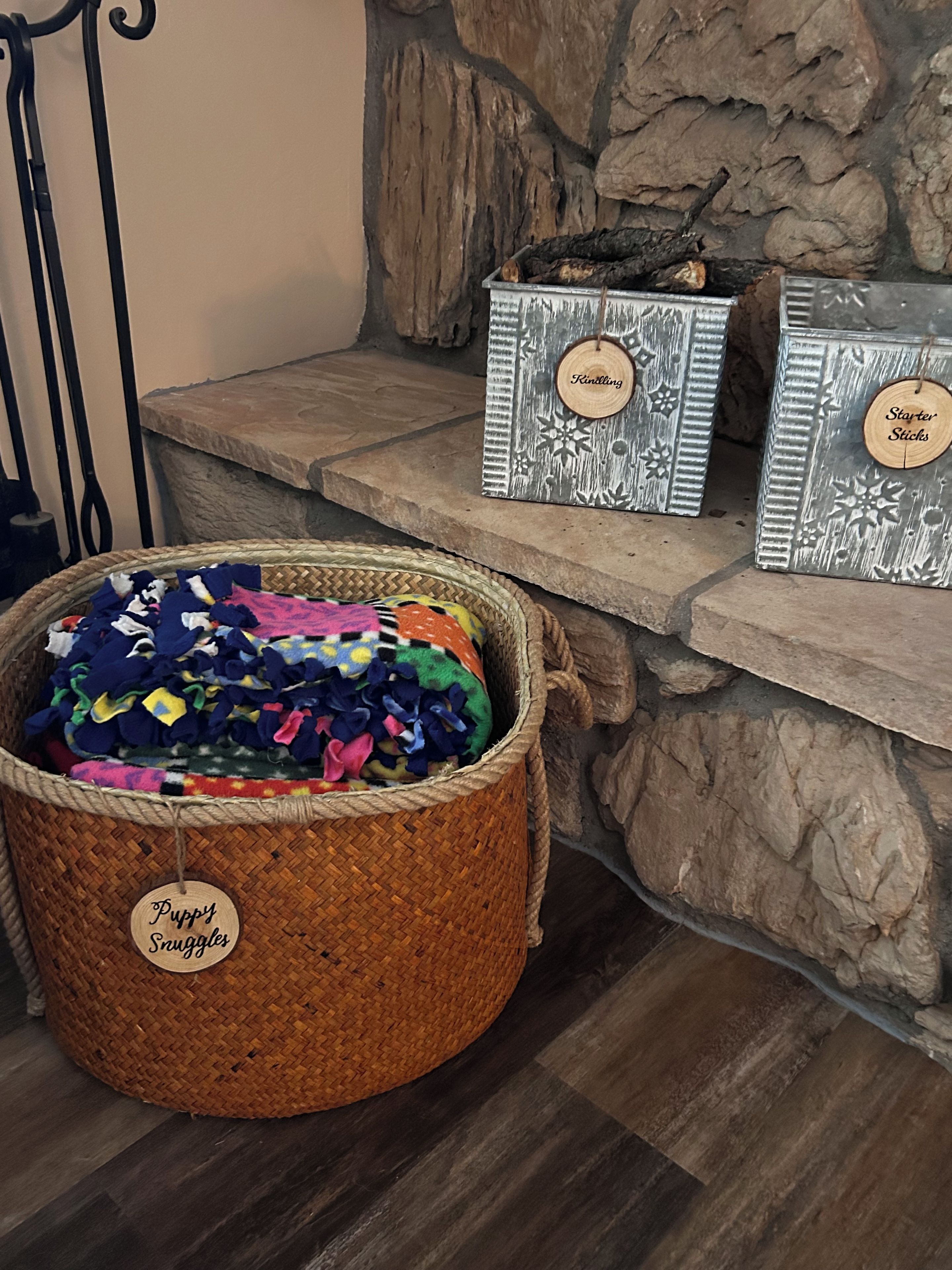 A wicker basket labeled 'Puppy Snuggles' filled with colorful toys, alongside two metal boxes with 'Kintling' and 'Starter Sticks' labels.