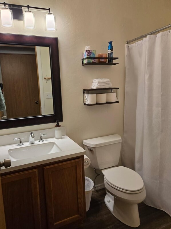 A bathroom with a white sink, a toilet, a shower curtain, and shelves with toiletries. - Nestled in the trees, family cabin room for 8, open for fall break & hunters! (Nutrioso)