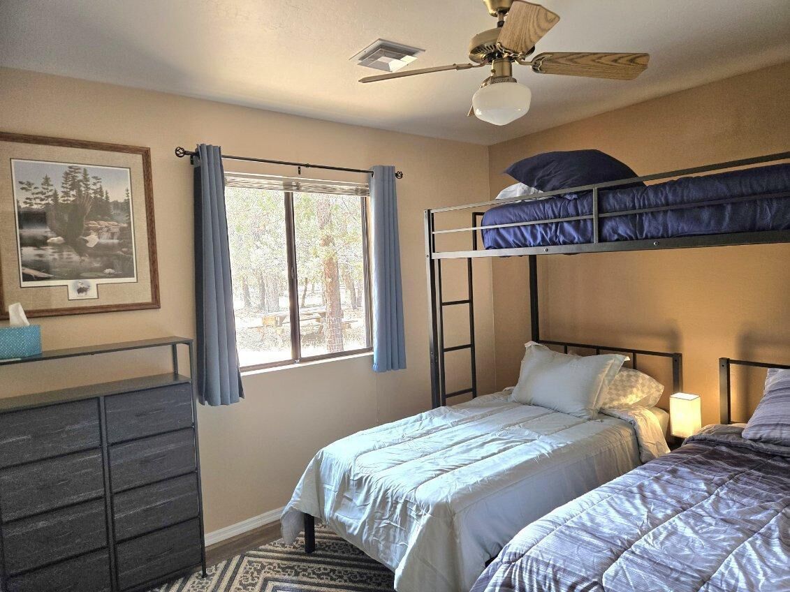 A bedroom with two beds, a ceiling fan, a window with curtains, a dresser, and a framed picture on the wall.