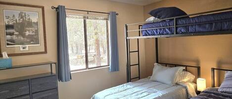 A bedroom with two beds, a ceiling fan, a window with curtains, a dresser, and a framed picture on the wall.