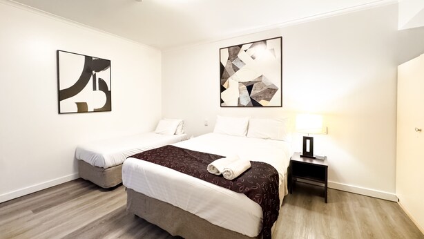 Une chambre d’hôtel avec deux lits, une table de chevet, une lampe et des œuvres d’art abstraites accrochées au mur.