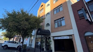 Un immeuble à plusieurs étages, doté d’un auvent noir sur lequel est inscrit le numéro 259, une entrée de garage et un ciel bleu dégagé.