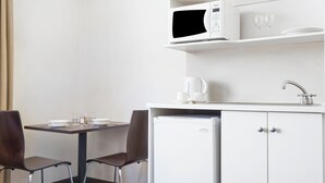 Une petite cuisine équipée d’un four à micro-ondes, d’une machine à café et d’un évier. Elle comprend également un petit réfrigérateur et une table à manger avec deux chaises.