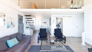 Amplia sala de estar con sofá, dos sillones, una mesa de centro de vidrio y una escalera que lleva a un nivel superior.