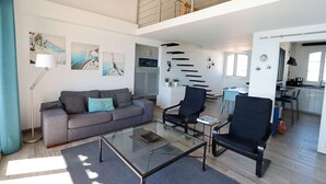 Una sala de estar moderna con un sofá, dos sillones, una mesa de centro de vidrio y obras de arte en las paredes.