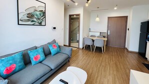 A modern living room with a grey sofa, a white coffee table, and a dining area with a wooden table and chairs. - Vinhomes Skylake (Hanoi)