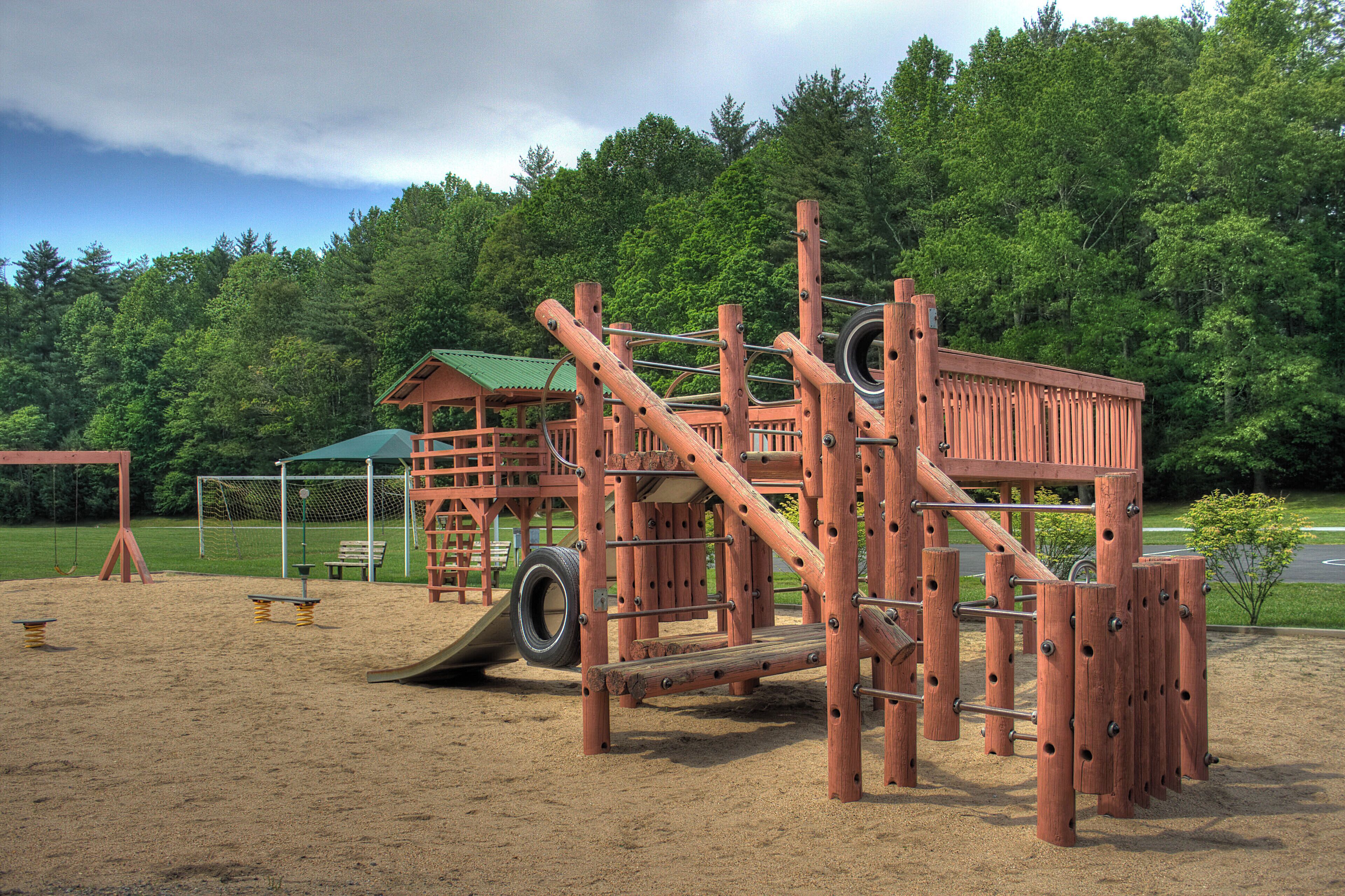 A playground with a wooden climbing structure, a slide, and a tire swing.