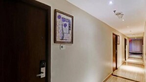 Un couloir d’hôtel avec une porte en bois, une œuvre d’art encadrée accrochée au mur et un couloir bien éclairé.