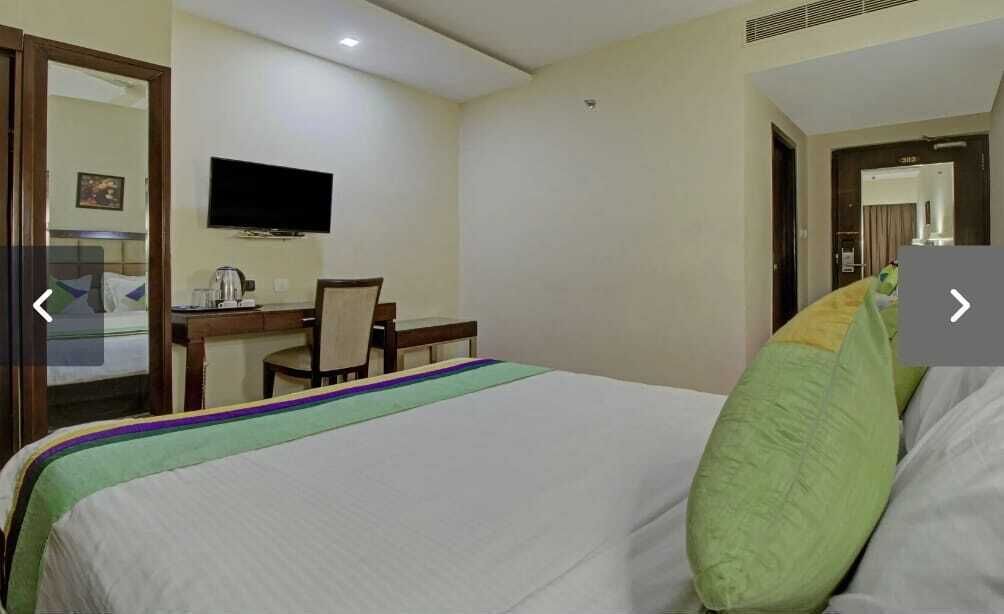 A hotel room with a bed, a desk, a chair, and a television on the wall.