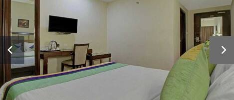 A hotel room with a bed, a desk, a chair, and a television on the wall.