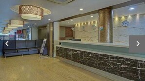 Un espace d’accueil d’hôtel avec un comptoir en marbre, un canapé et des luminaires décoratifs au plafond.