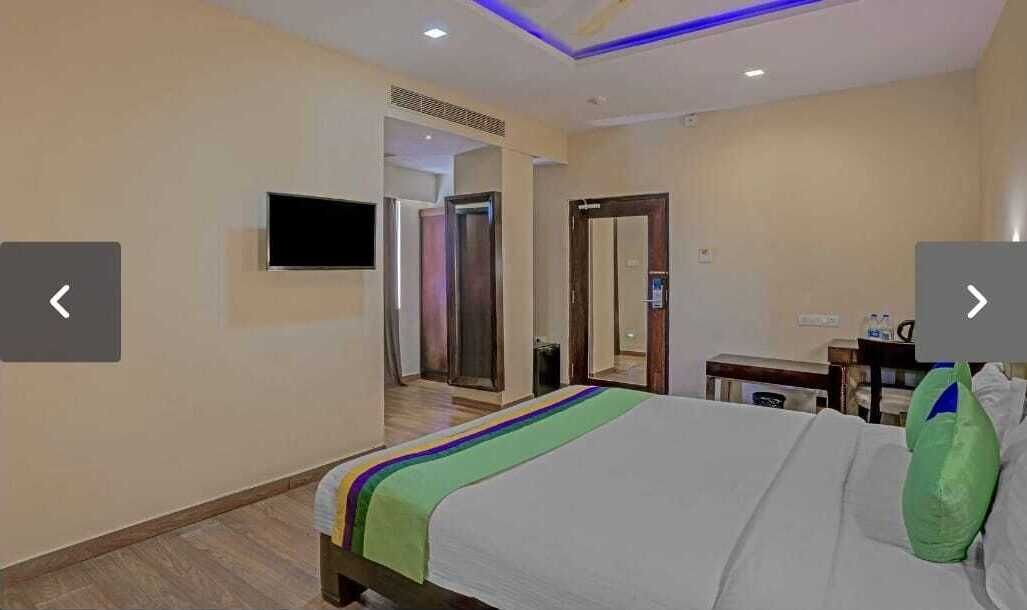 Una habitación de hotel con una cama, televisión montada en la pared, escritorio y espejo.