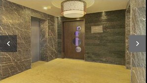 Un couloir aux murs de marbre, une porte en bois ornée de motifs circulaires et un sol recouvert de moquette.