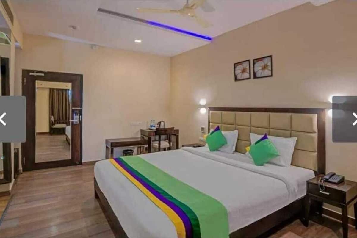 A hotel room with a large bed, a desk, and a chair. There is a ceiling fan and a door leading to another room.