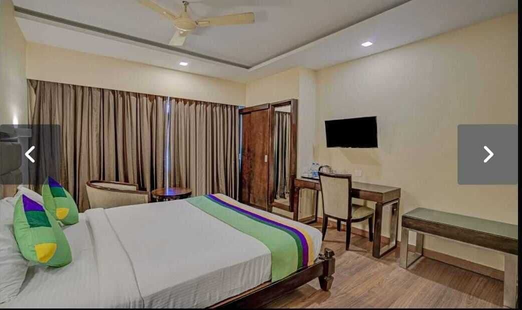 Una habitación de hotel con cama, escritorio, silla, televisor y ventilador de techo.