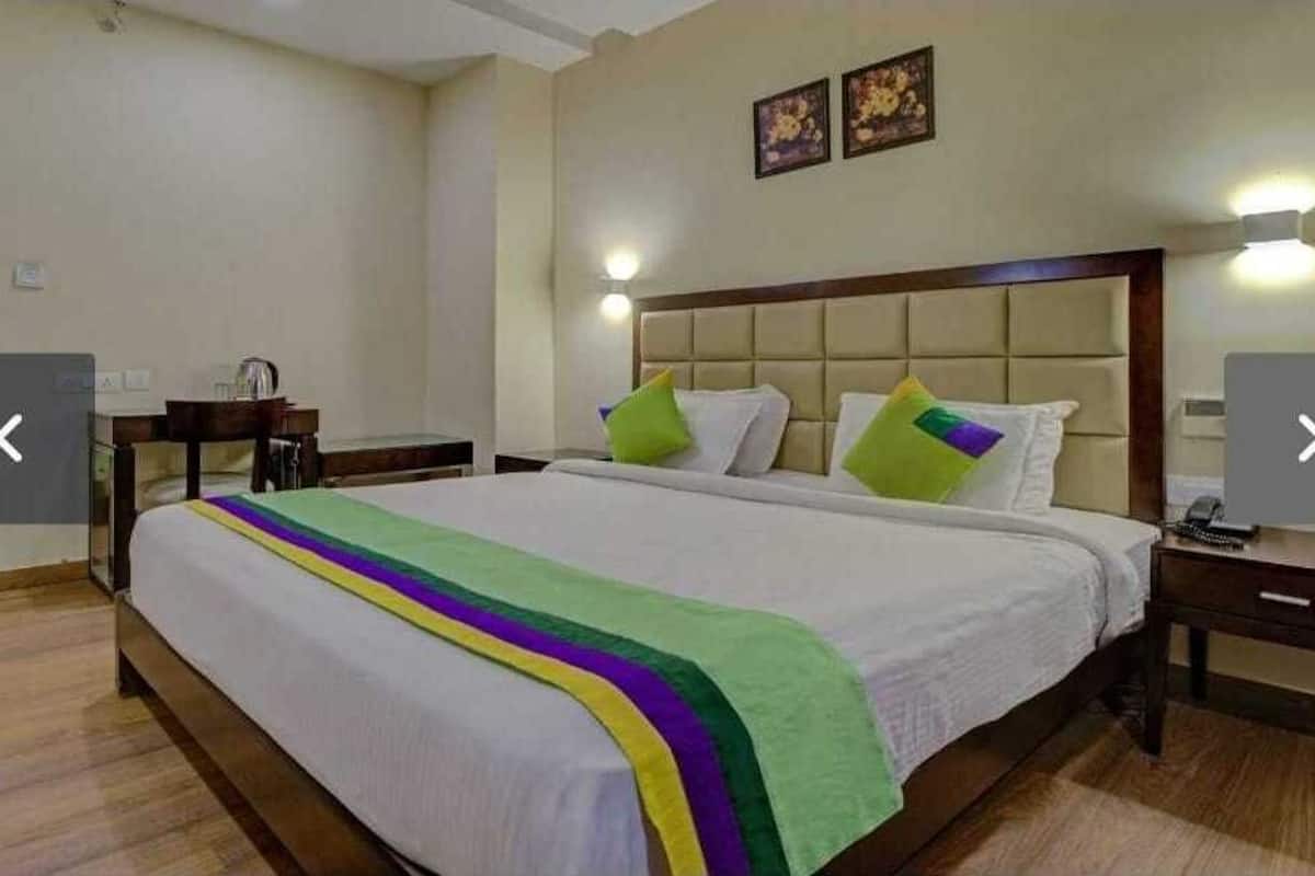A hotel room with a large bed, a wooden nightstand, a desk, and two wall-mounted lamps.