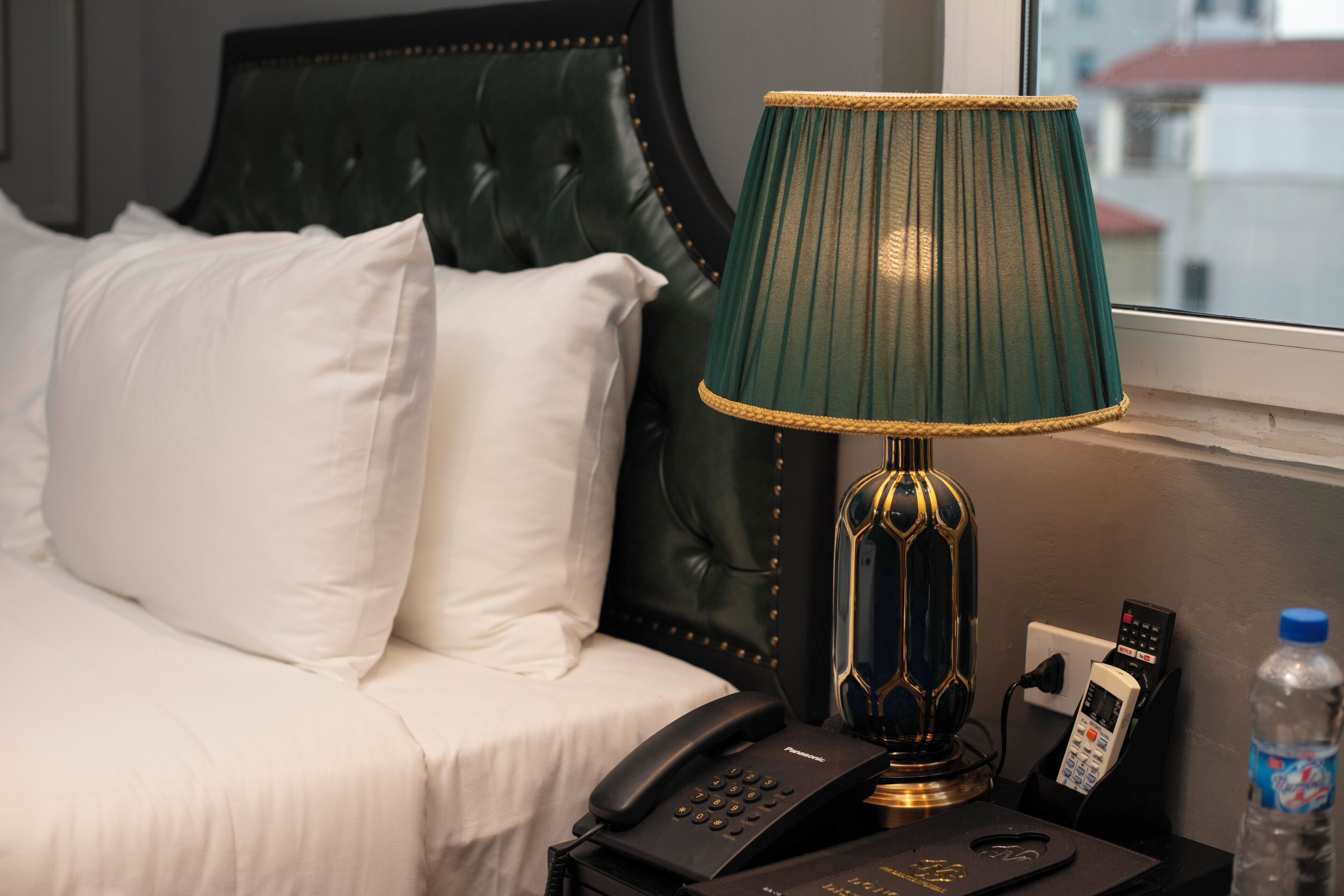 Una habitación de hotel con cama, una lámpara verde, un teléfono y una botella de agua.