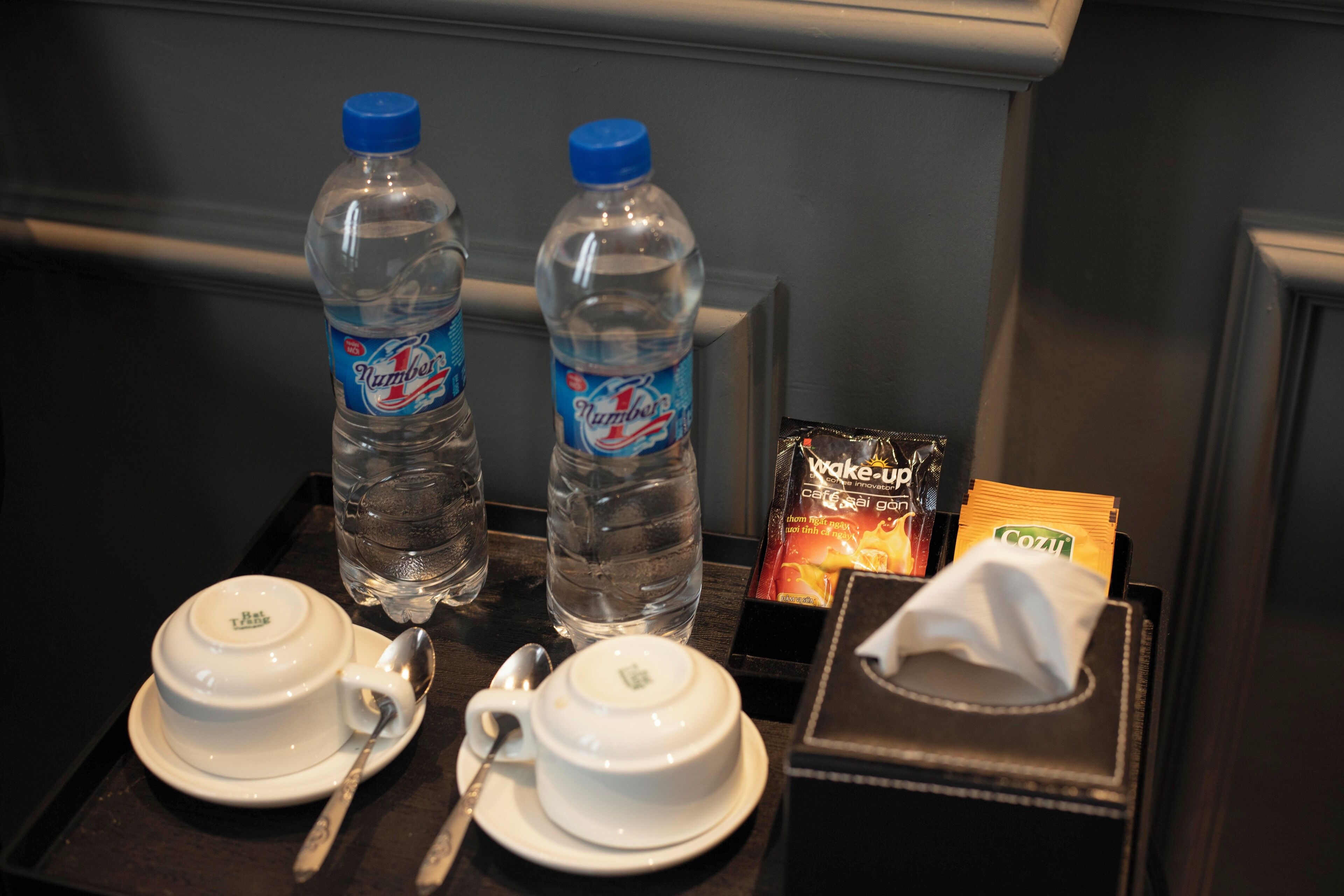 Ein Tablett mit zwei weißen Tassen, zwei Wasserflaschen, einer Papiertütenbox und einer Snackpackung.