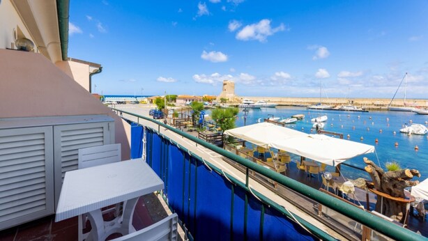 A balcony with a view of a marina, including boats and a historic tower. - BILOCALE ACQUAMARINA - BILOCALE ACQUAMARINA (Marciana Marina)