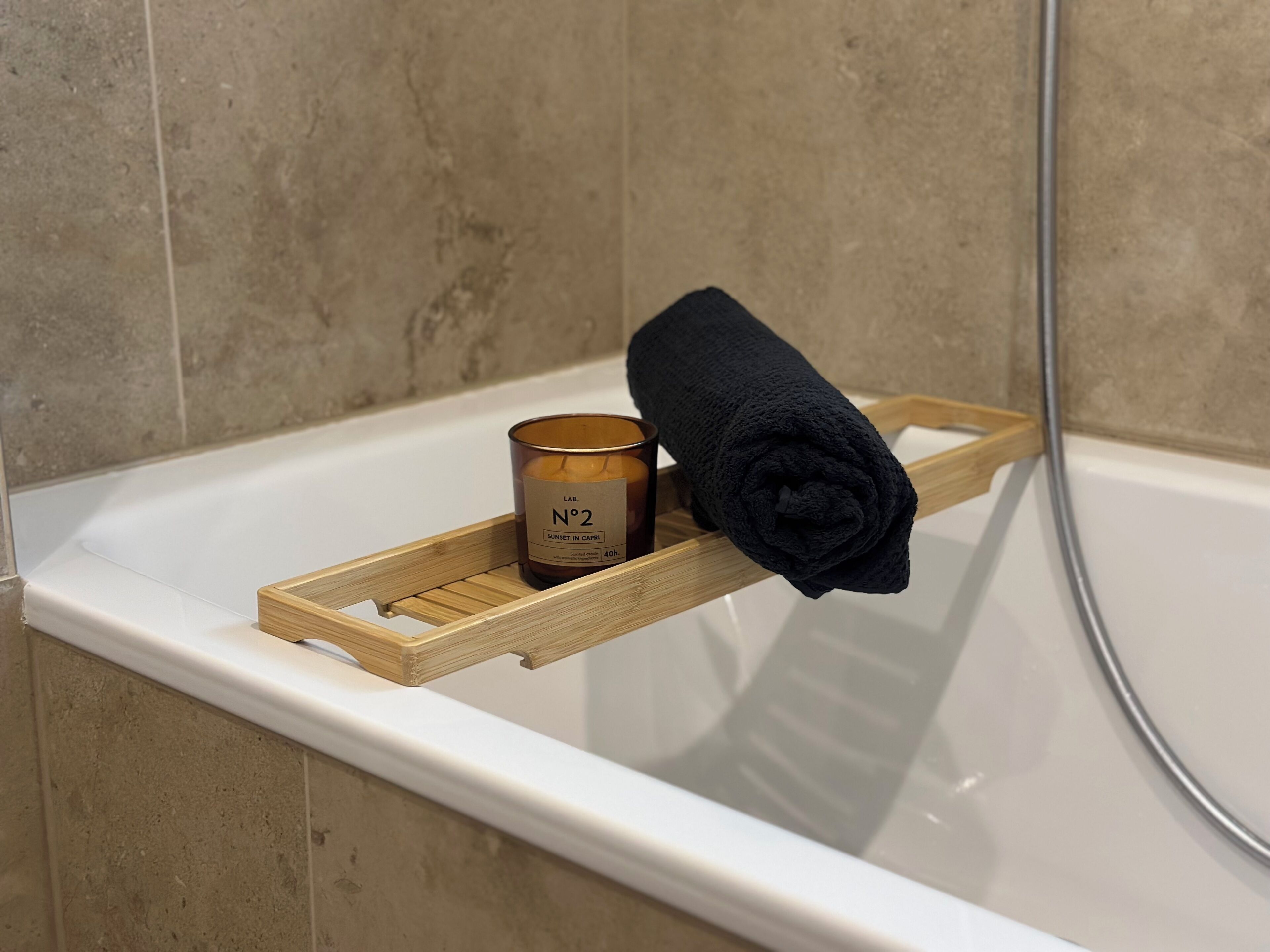 A bathroom with a wooden tray holding a candle and a rolled towel on a white bathtub.