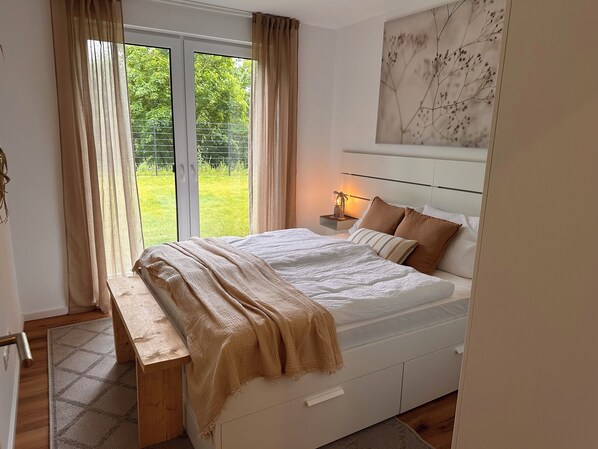 Une chambre à coucher avec un lit, une table de chevet et une vue sur un jardin verdoyant par la fenêtre.