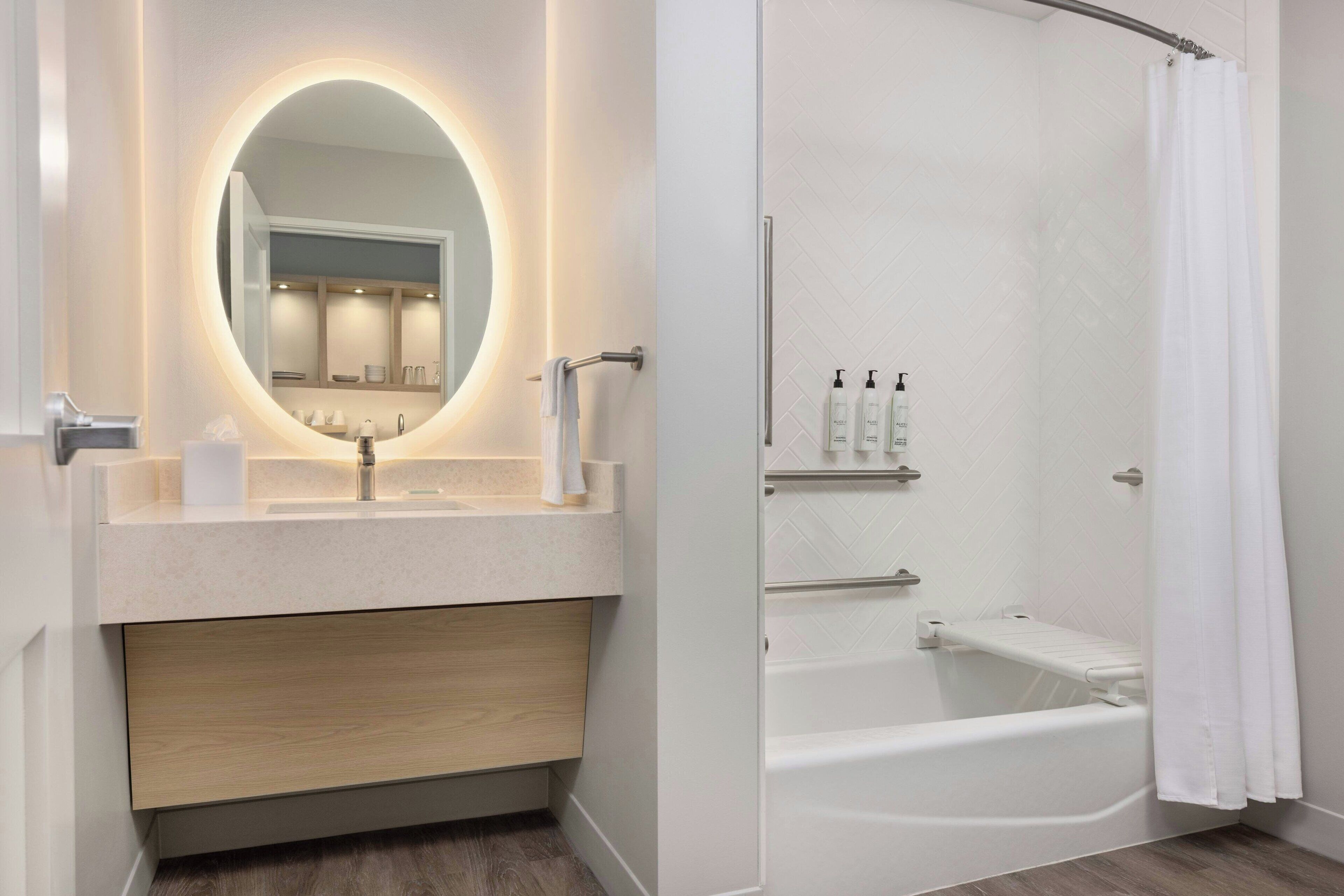 Un baño moderno con un espejo redondo, un lavamanos, una bañera y una cortina de ducha.