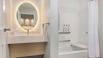 Un baño moderno con un espejo redondo, un lavamanos, una bañera y una cortina de ducha.