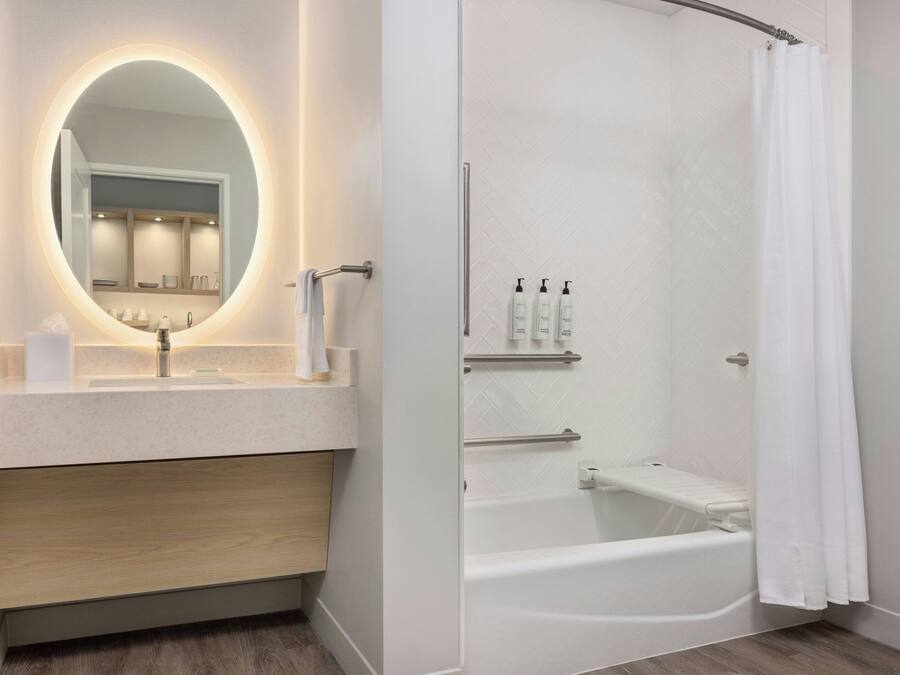 Un baño moderno con un espejo redondo, un lavamanos, una bañera y una cortina de ducha.