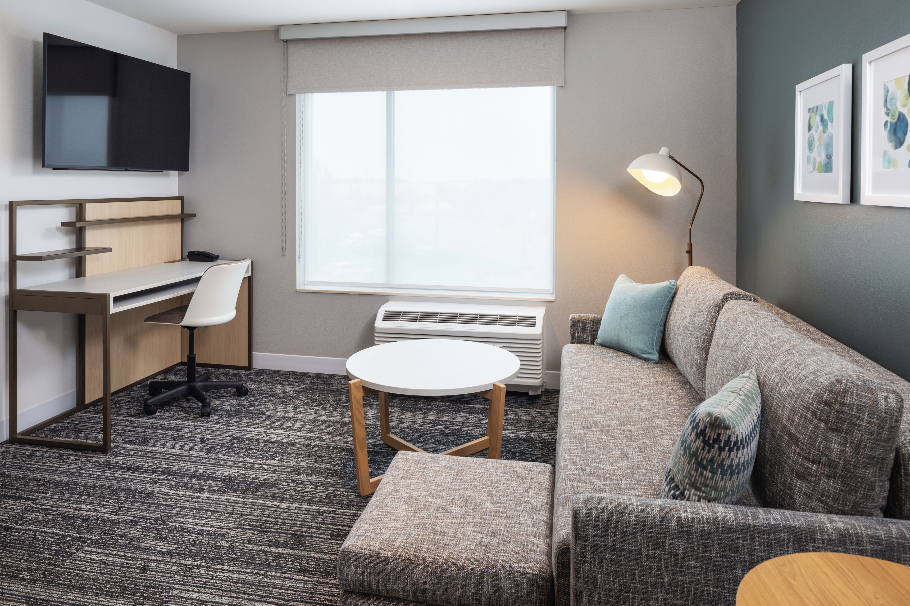 Ein modernes Hotelzimmer mit Schreibtisch, Stuhl, Sofa und Hocker.