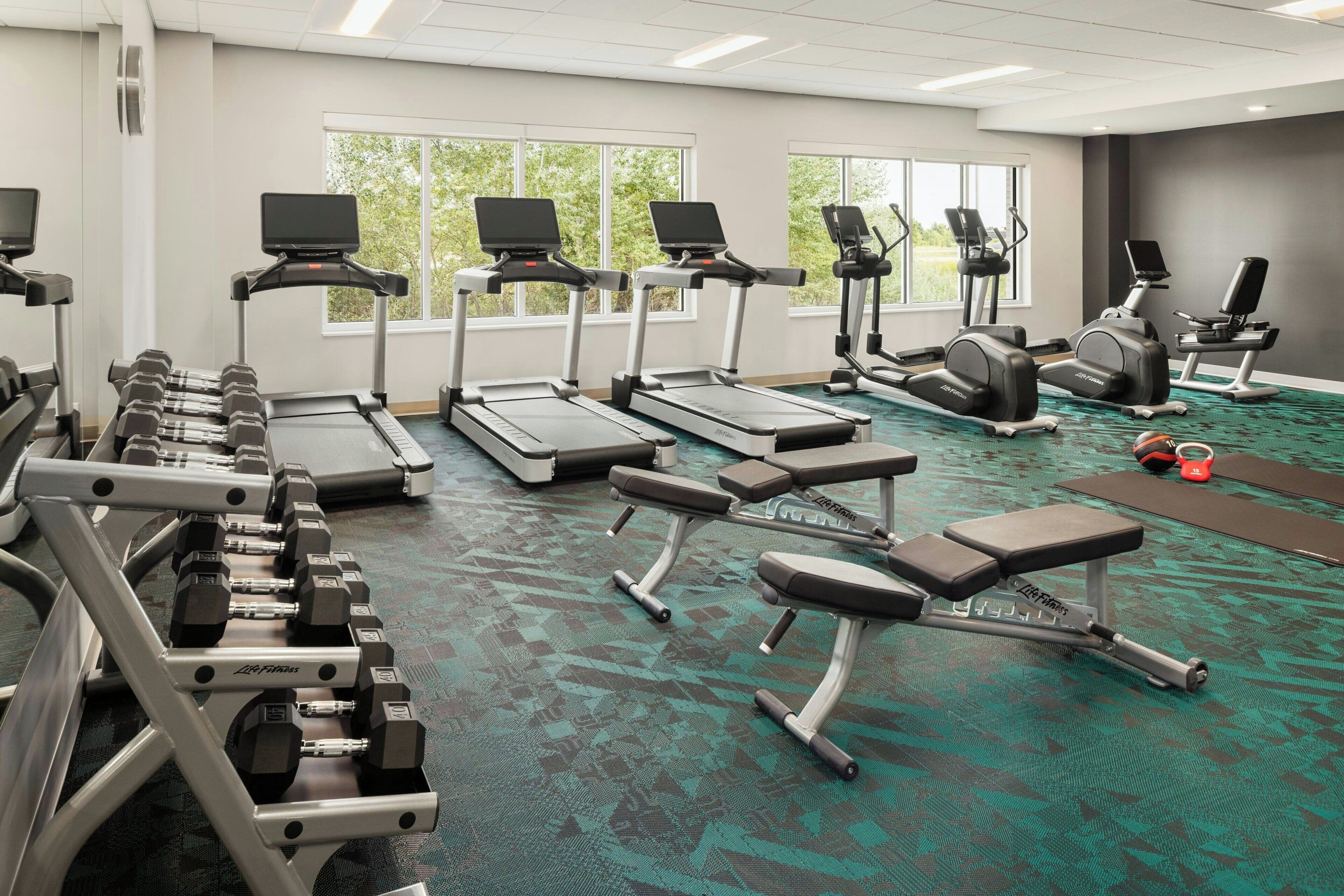A gym with treadmills, dumbbells, and weight benches.