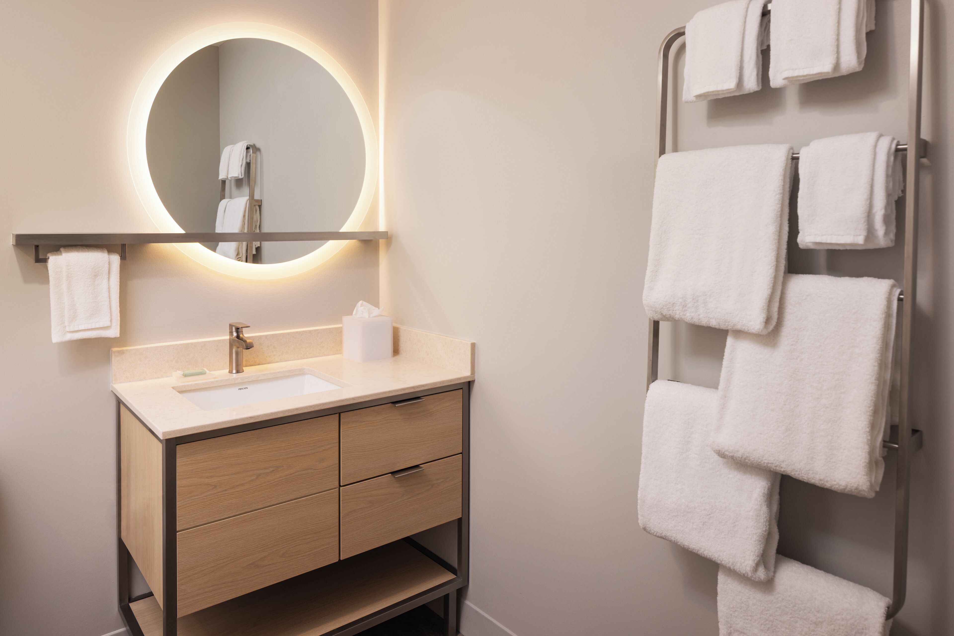 Ein modernes Badezimmer mit rundem Spiegel, Waschbecken und Handtuchhalter.