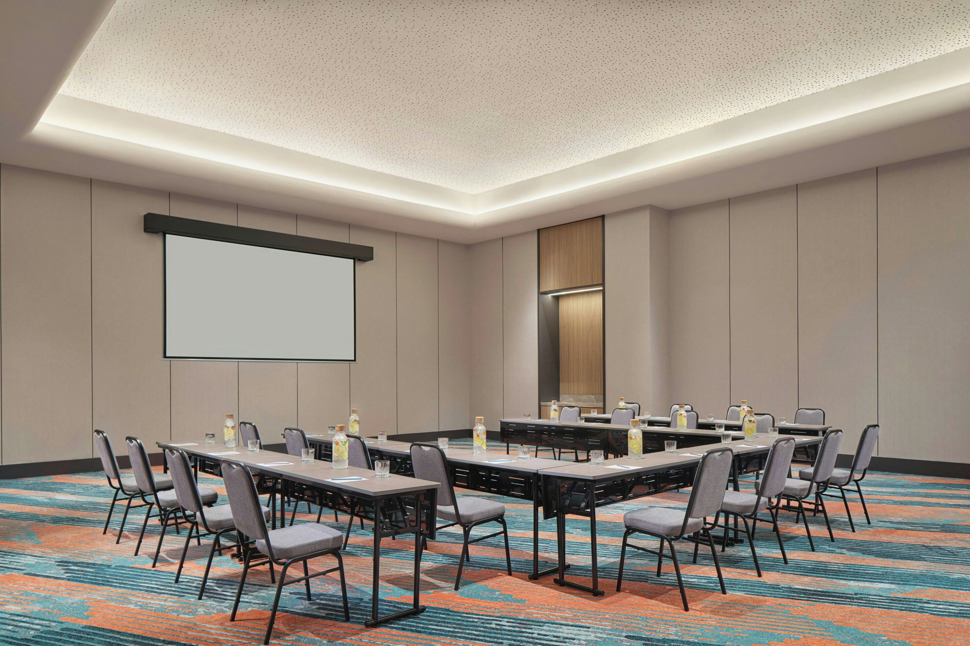 A conference room with a large screen, multiple tables, and chairs.