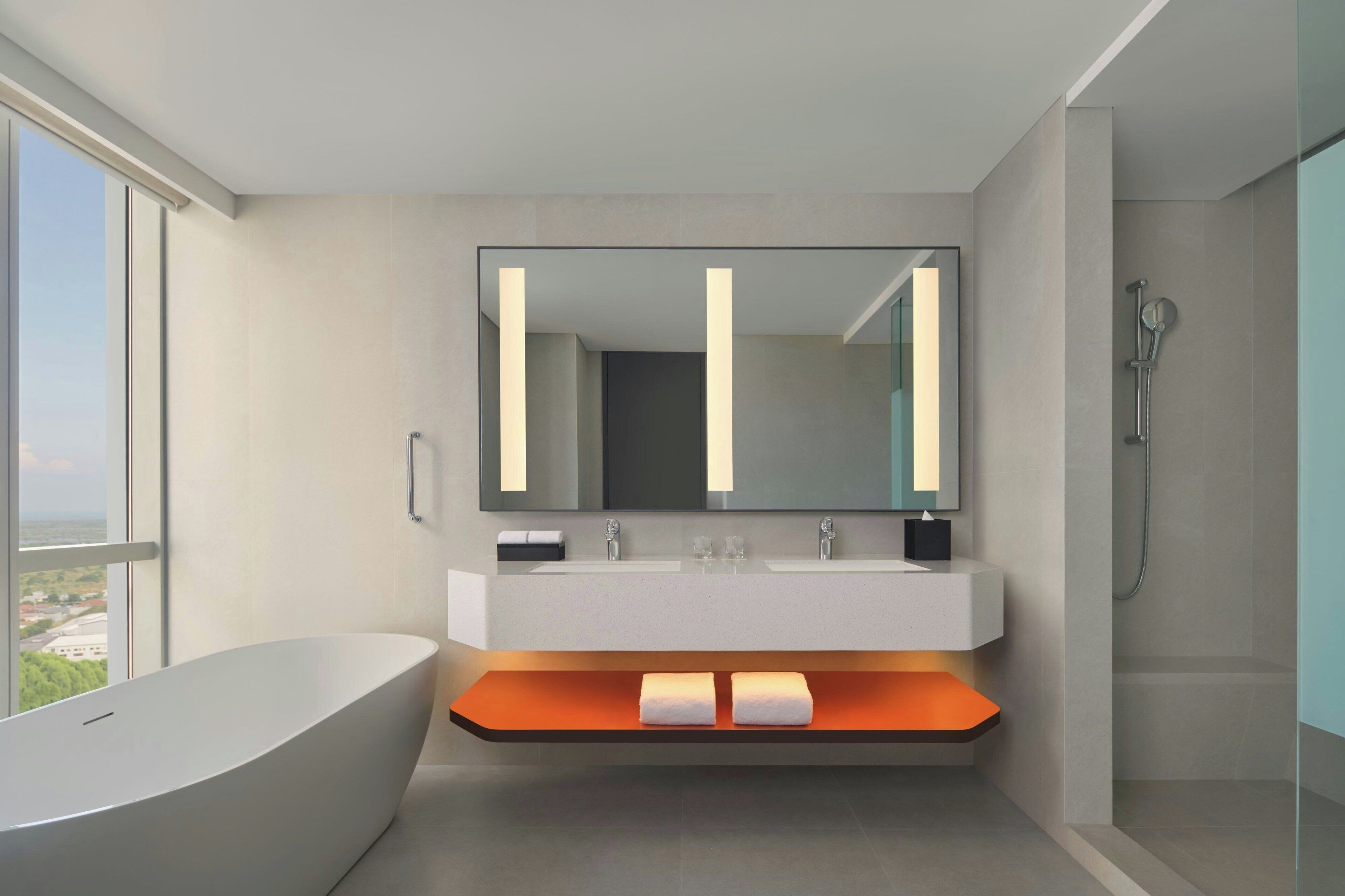 Un baño moderno con una bañera independiente, un espejo grande y una ducha.