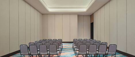 A conference room with rows of chairs, a patterned carpet, and a ceiling with a light fixture.