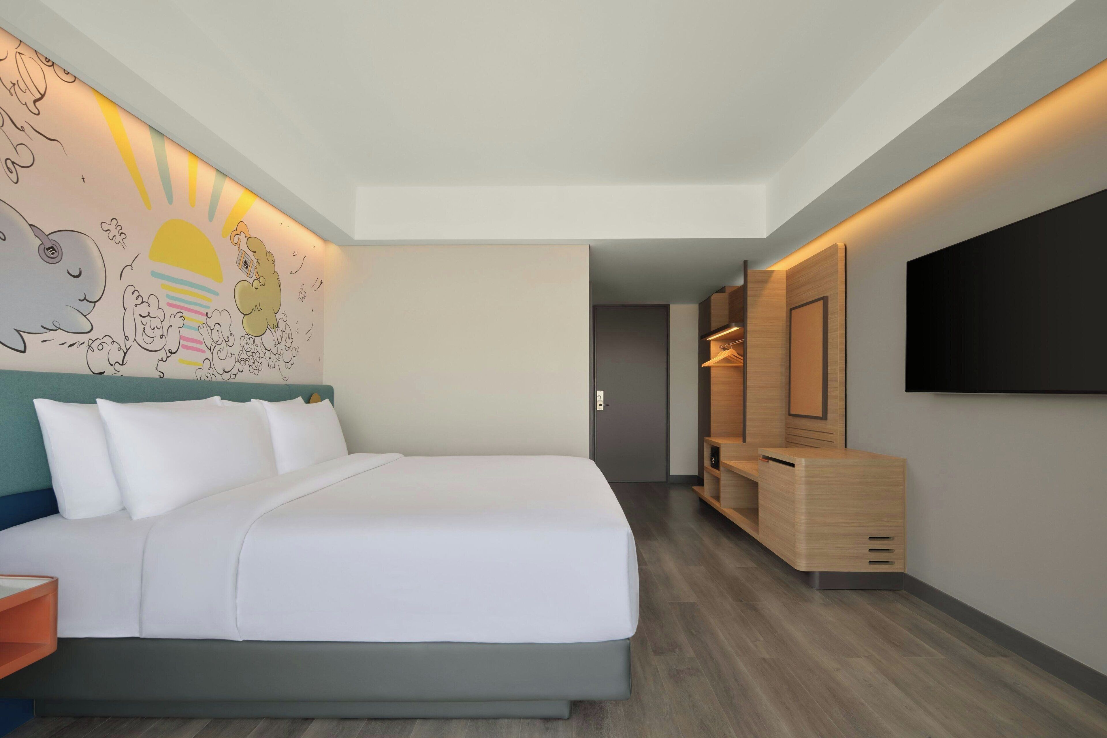 Une chambre d’hôtel moderne dotée d’un grand lit, d’une fresque murale, d’un téléviseur et de rangements intégrés en bois.