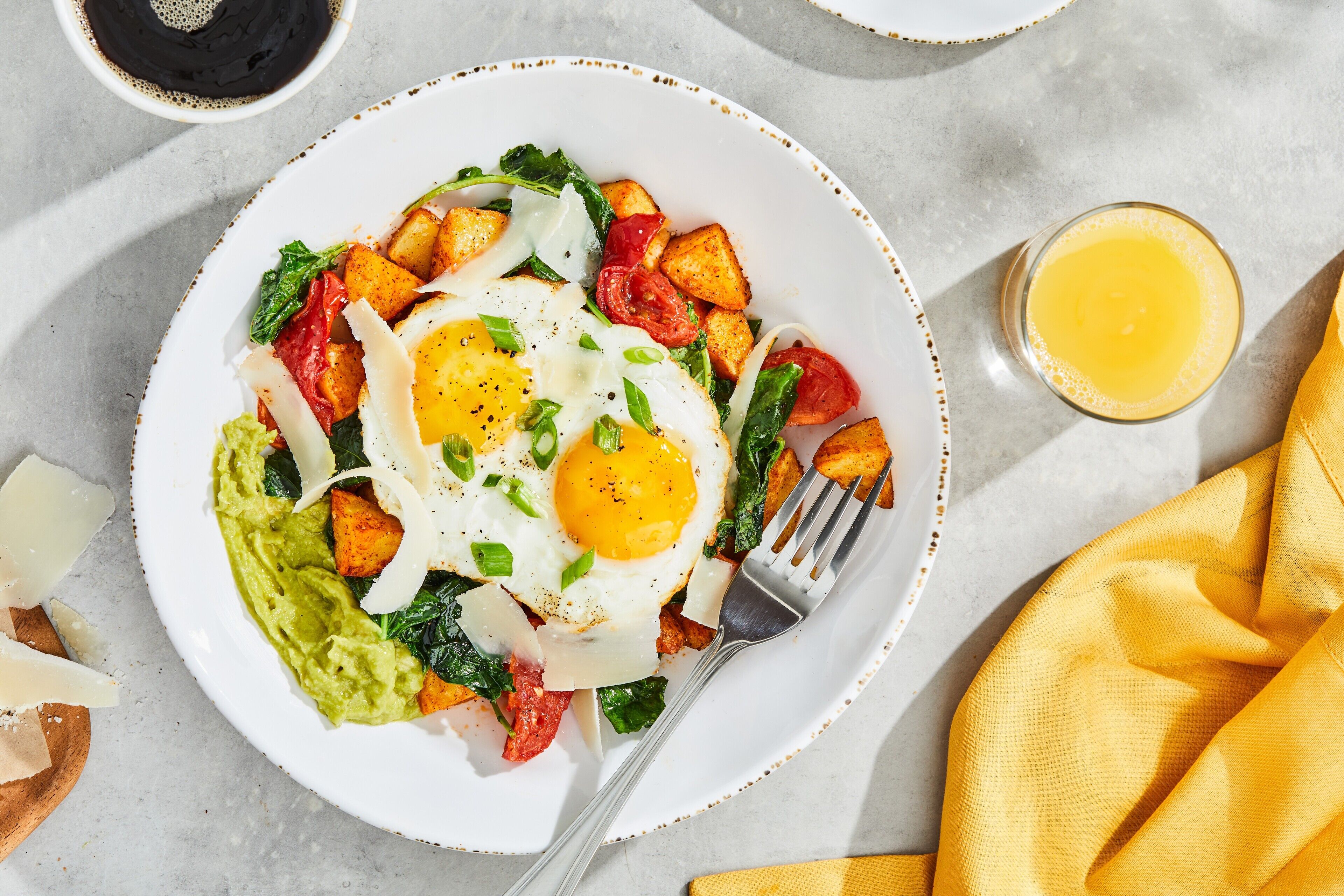 A plate of food with eggs, potatoes, and greens, a fork, and a glass of orange juice.