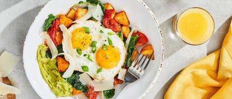 A plate of food with eggs, potatoes, and greens, a fork, and a glass of orange juice.