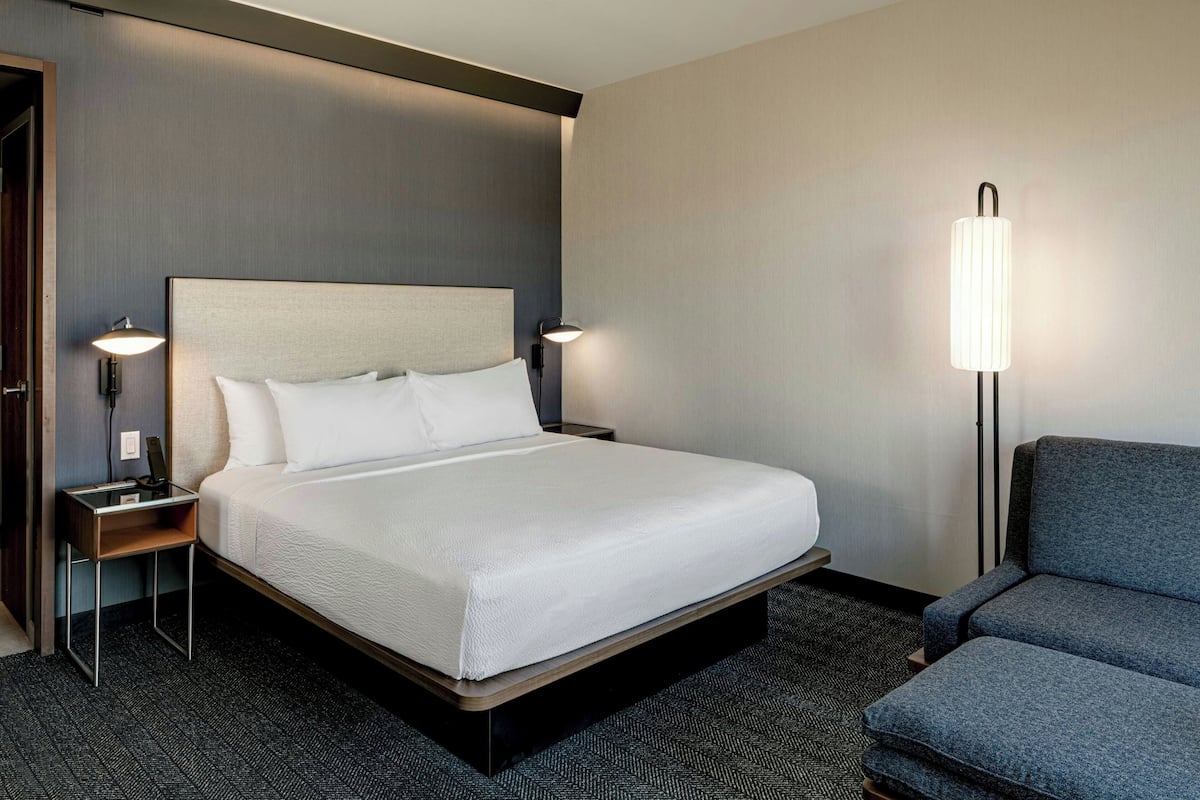 Una habitación de hotel con una cama grande, dos mesitas de noche, una silla y una lámpara de pie.