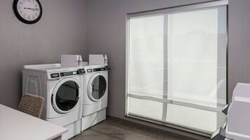 A laundry room with two front-loading washing machines, a wall clock, and a large window.