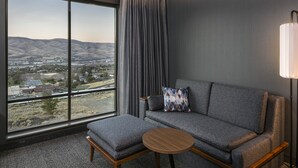 A modern hotel room with a large window offering a view of a valley, a grey sofa with a patterned pillow, and a small wooden table. - Courtyard by Marriott Lewiston (Lewiston)