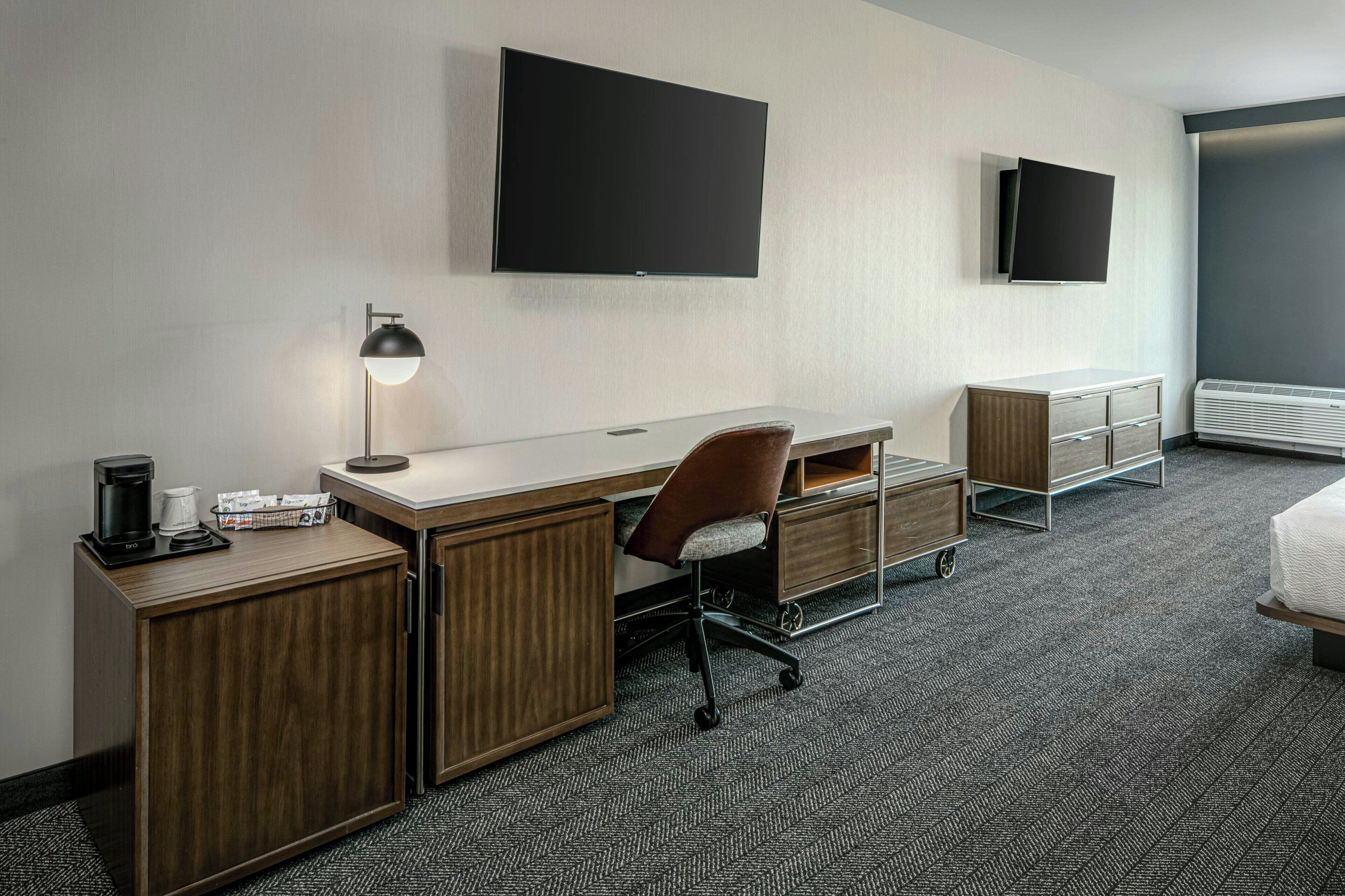 Une chambre d’hôtel équipée d’un bureau, d’une chaise et de deux écrans de télévision fixés au mur.