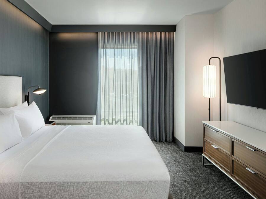 A hotel room with a large bed, a dresser, a flat-screen TV, and a window with curtains.