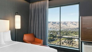 A hotel room with a bed, a chair, a lamp, a large window with a view of mountains and a town. - Courtyard by Marriott Lewiston (Lewiston)