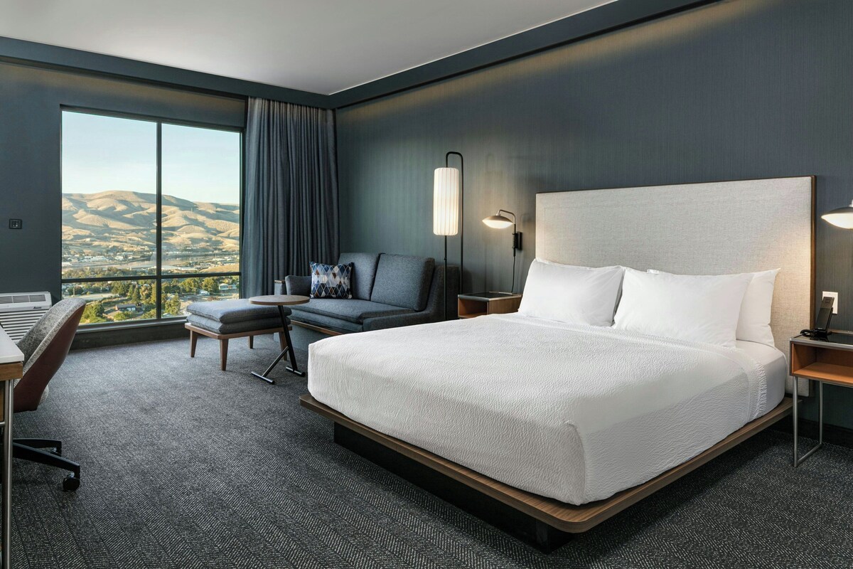 Un hotel moderno con una cama grande, un escritorio, una silla y vistas a las colinas.