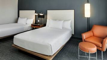 Hotellihuone, jossa on kaksi sänkyä, yöpöytä, lamppu ja nahkainen nojatuoli.
