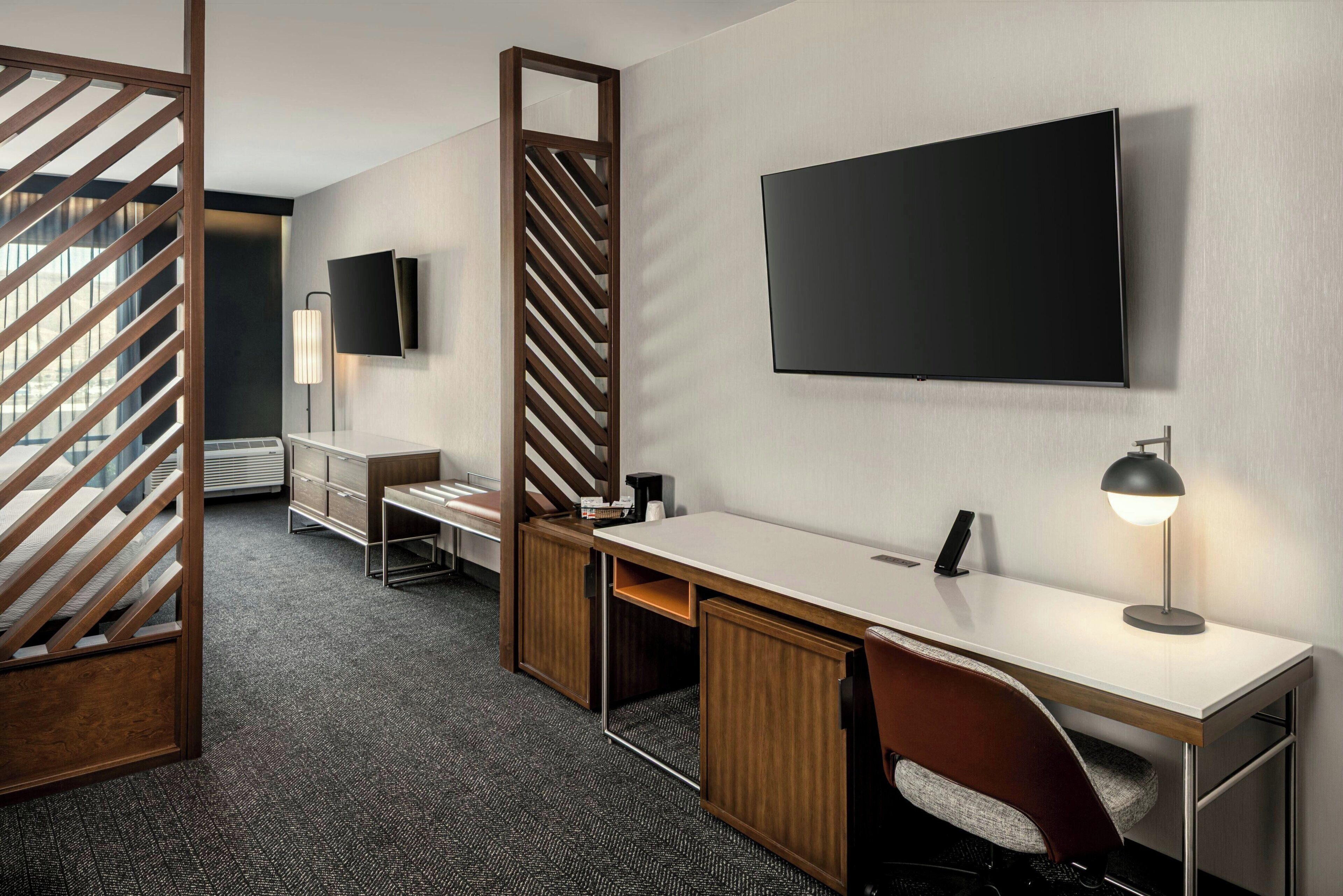 Een moderne hotelkamer met een bureau, stoel, televisie en een scheidingswand met een houten lattenstructuur.