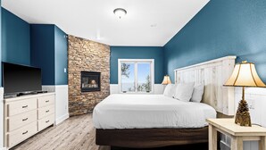 A bedroom with a stone accent wall, a large bed, a TV, and a window with a view. - Breathtaking Lake Views | 2BR w/King Suite | Pools (Two Harbors)