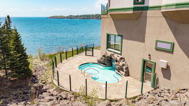 A pool with a natural rock design, surrounded by a stone deck, overlooking a body of water.