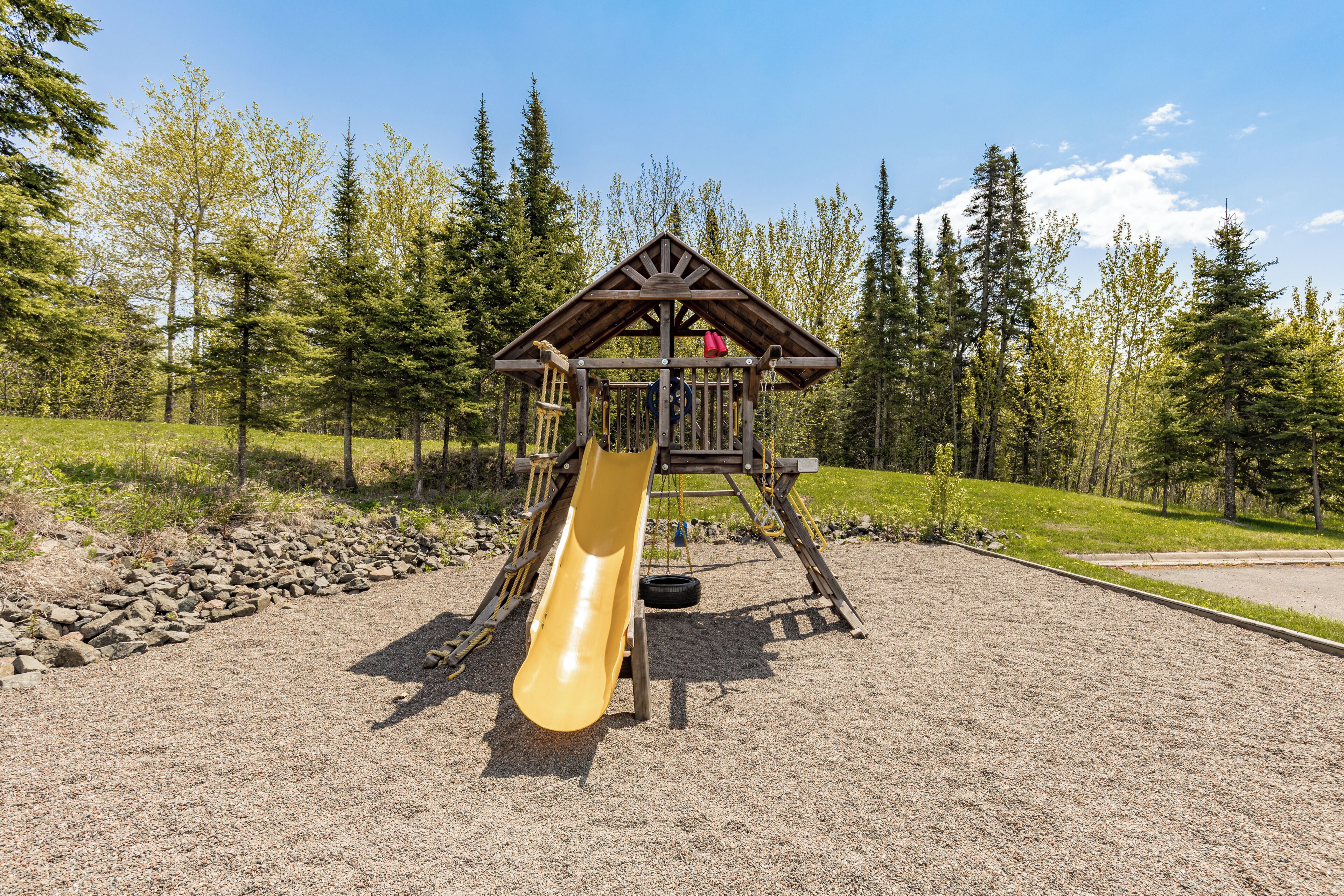 Un terrain de jeux équipé d’un toboggan et de structures d’escalade, entouré d’arbres et recouvert de gravier.